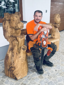 Holzbank mit einem Wildschwein und einer Eule mit der Motorsäge geschnitzt von Markus Weigmann und mit ihm darauf sitzend