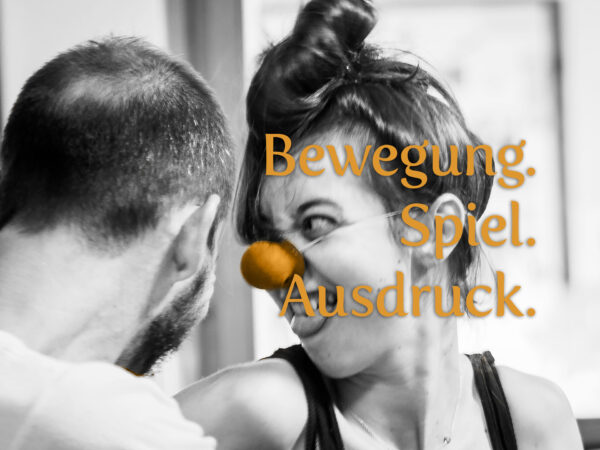 (Foto: Netty Kinsky) Eine Clownin mit roter Nase lacht herzlich, während eine Hand sanft ihre Wange berührt. Der orangefarbene Schriftzug 'Bewegung. Spiel. Ausdruck.' betont die lebendige und spielerische Atmosphäre des Pantomime-, Clownerie- & Stepptanz-Festivals.