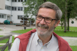 Karl A. Immervoll, Gesprächspartner beim Symposion des Pantomime-, Clownerie- & Stepptanz-Festivals „Bewegung. Spiel. Ausdruck.“, trägt eine Brille, einen graumelierten Bart und ein kariertes Hemd mit einem roten Pullover. Sein Lächeln strahlt Herzlichkeit und Engagement aus. (Foto: Erhart Hois)